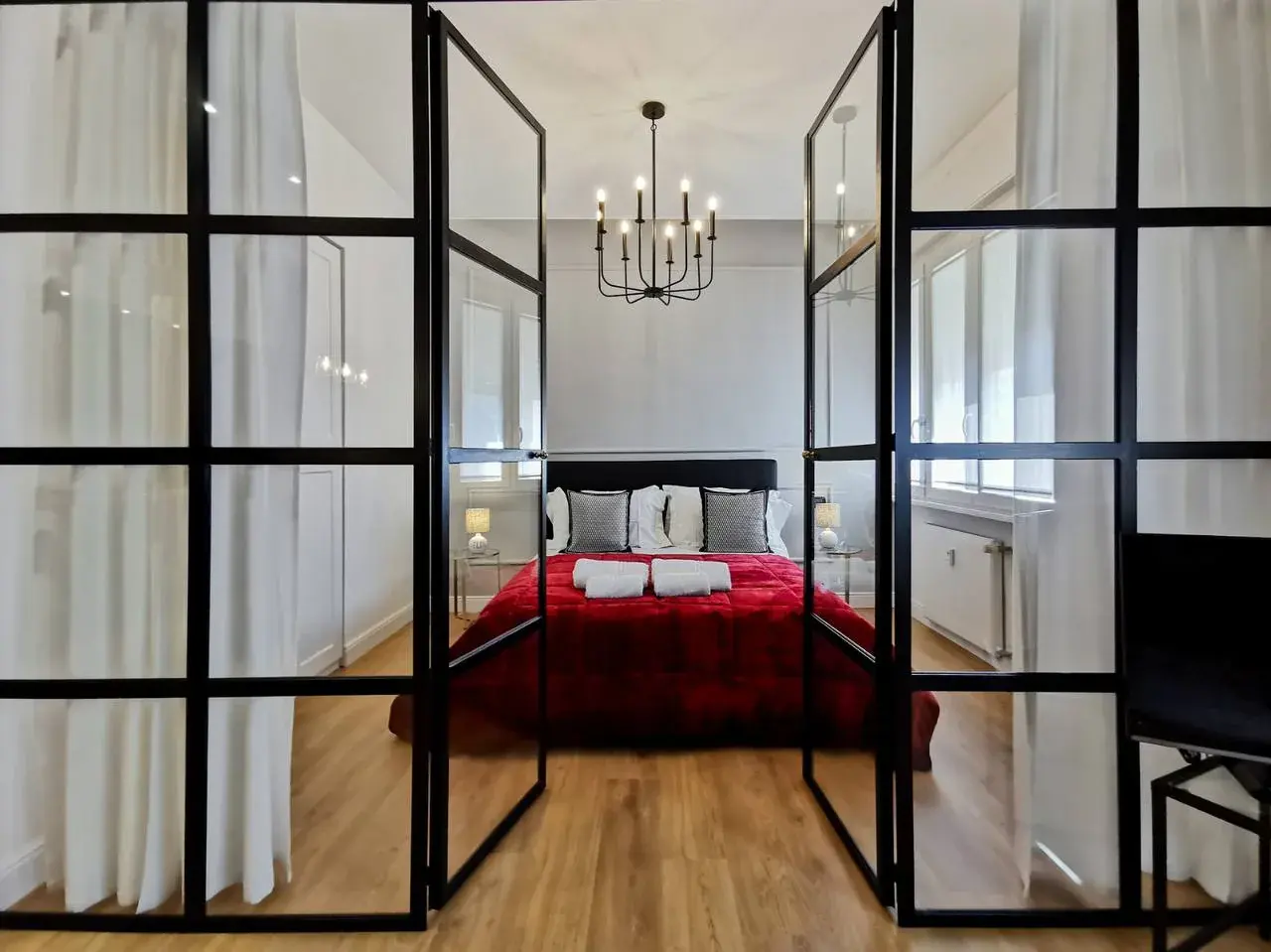 חדר שינה עם מיטה אדומה, מאחורי מחיצת זכוכית במסגרת שחורה